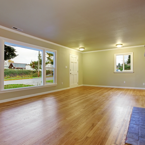 A bright living room with hardwood floors, large windows, and a white door