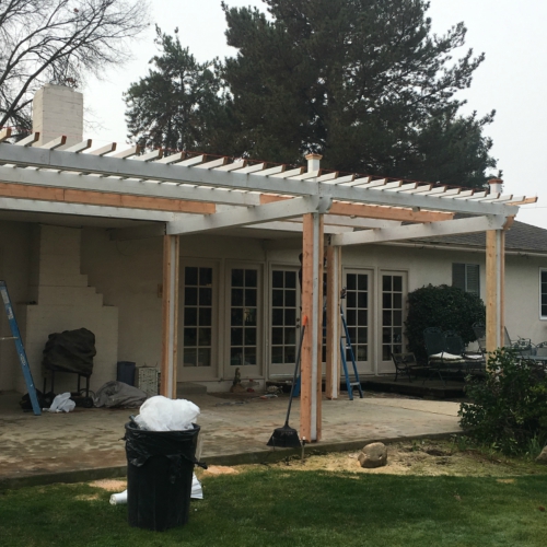 A pergola under construction with white wooden beams and posts