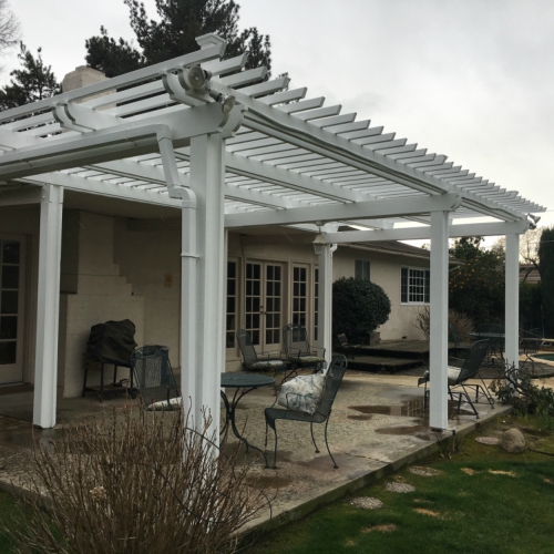 A white pergola with a lattice roof covering a patio area with chairs and a table