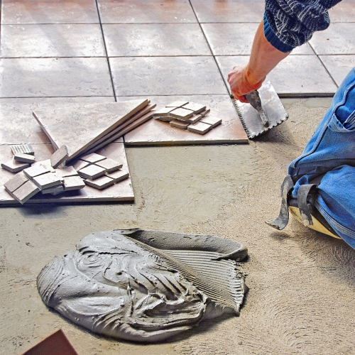 A person installing tiles on a floor using a trowel and mortar