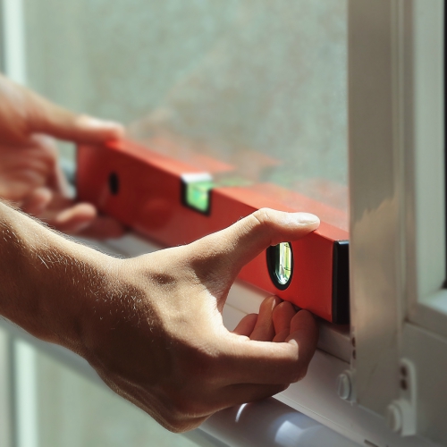 Close-up of a person's hands holding a red level tool against a window frame