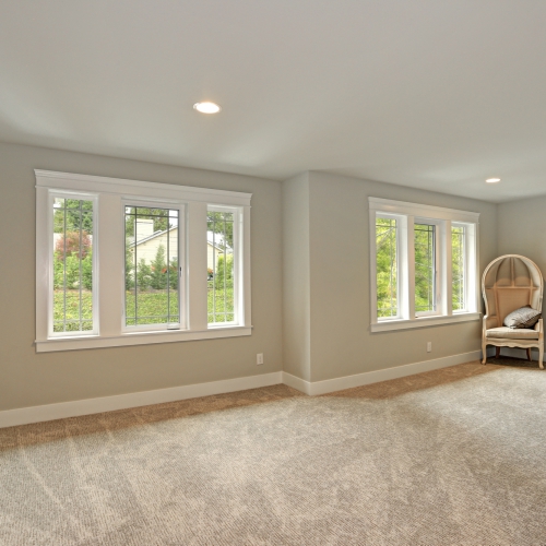 A carpeted room with large windows, white walls, and a single chair in the corner
