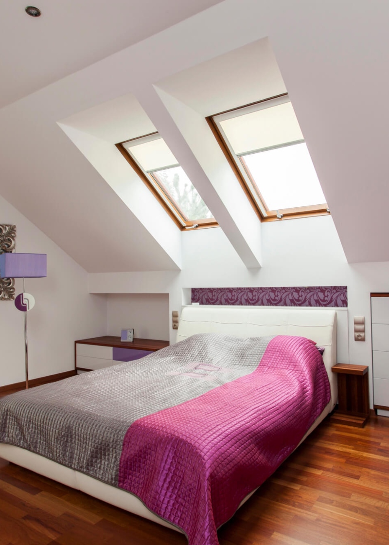 Modern bedroom with white walls, a colorful bedspread, and natural light from the skylights